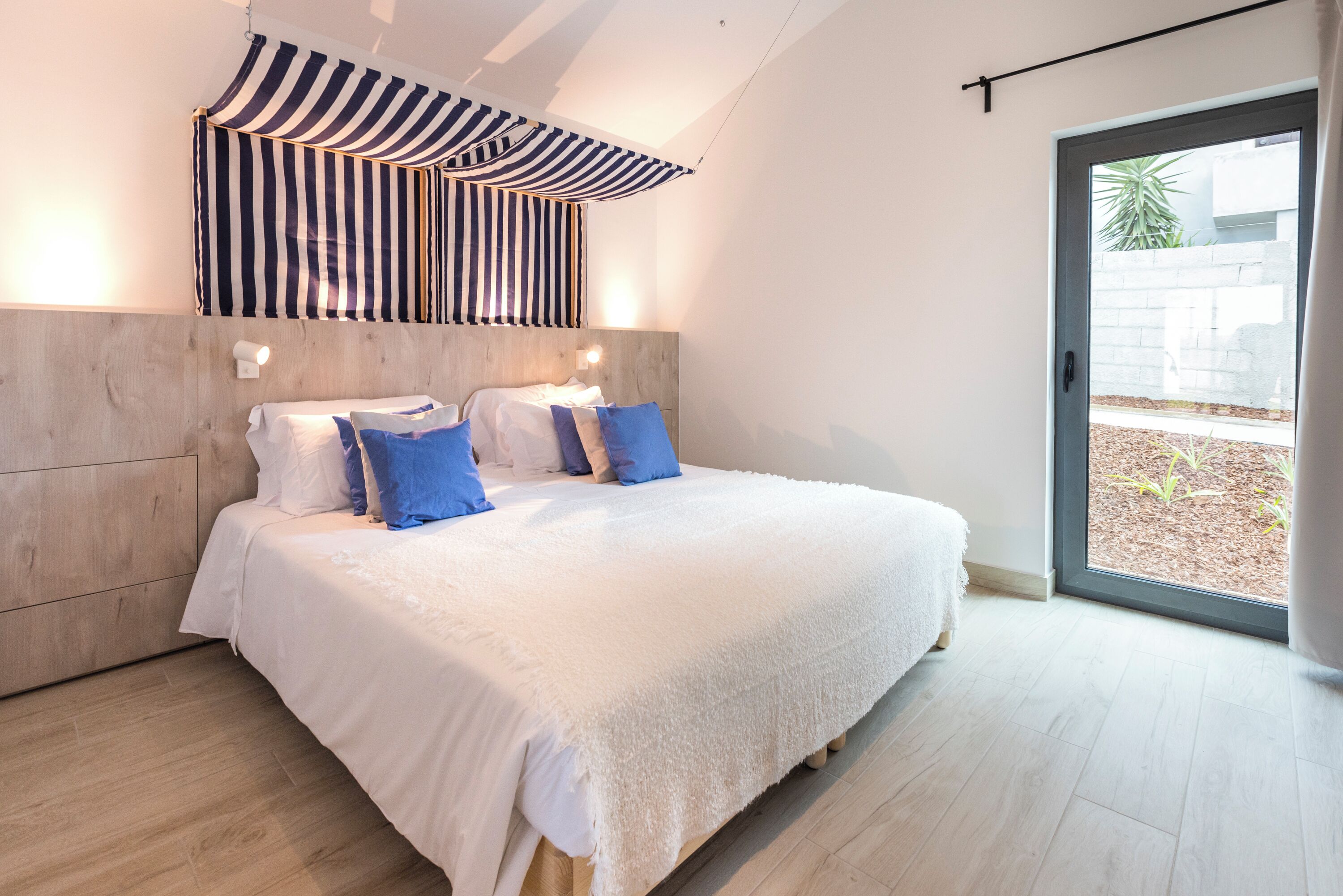 A bedroom with a large bed, a striped canopy, a wooden headboard, and a view of the outdoors through a glass door.
