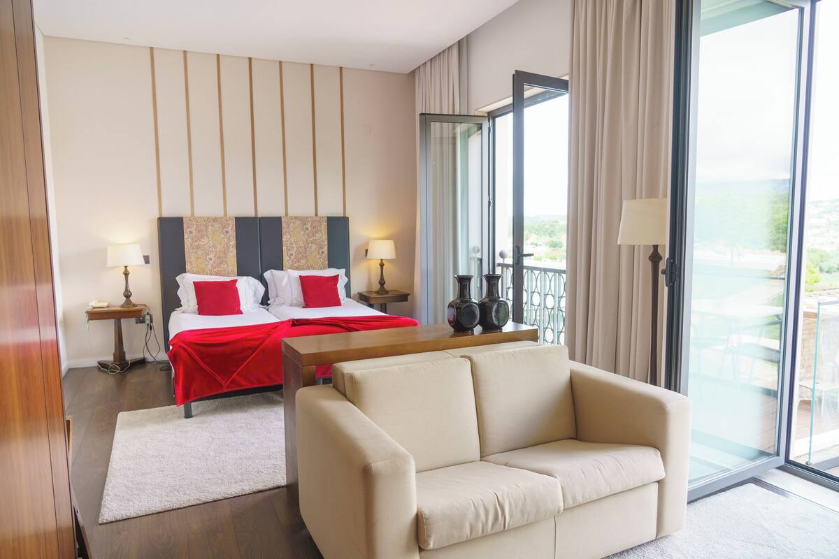 Una habitación de hotel con cama, sofá, escritorio y vistas al exterior.
