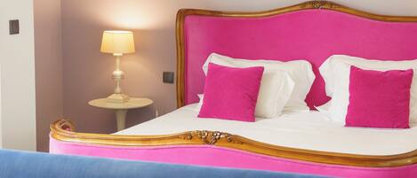 A bed with a pink headboard and white bedding, a small bedside table with a lamp, and a blue sofa with a pink pillow.
