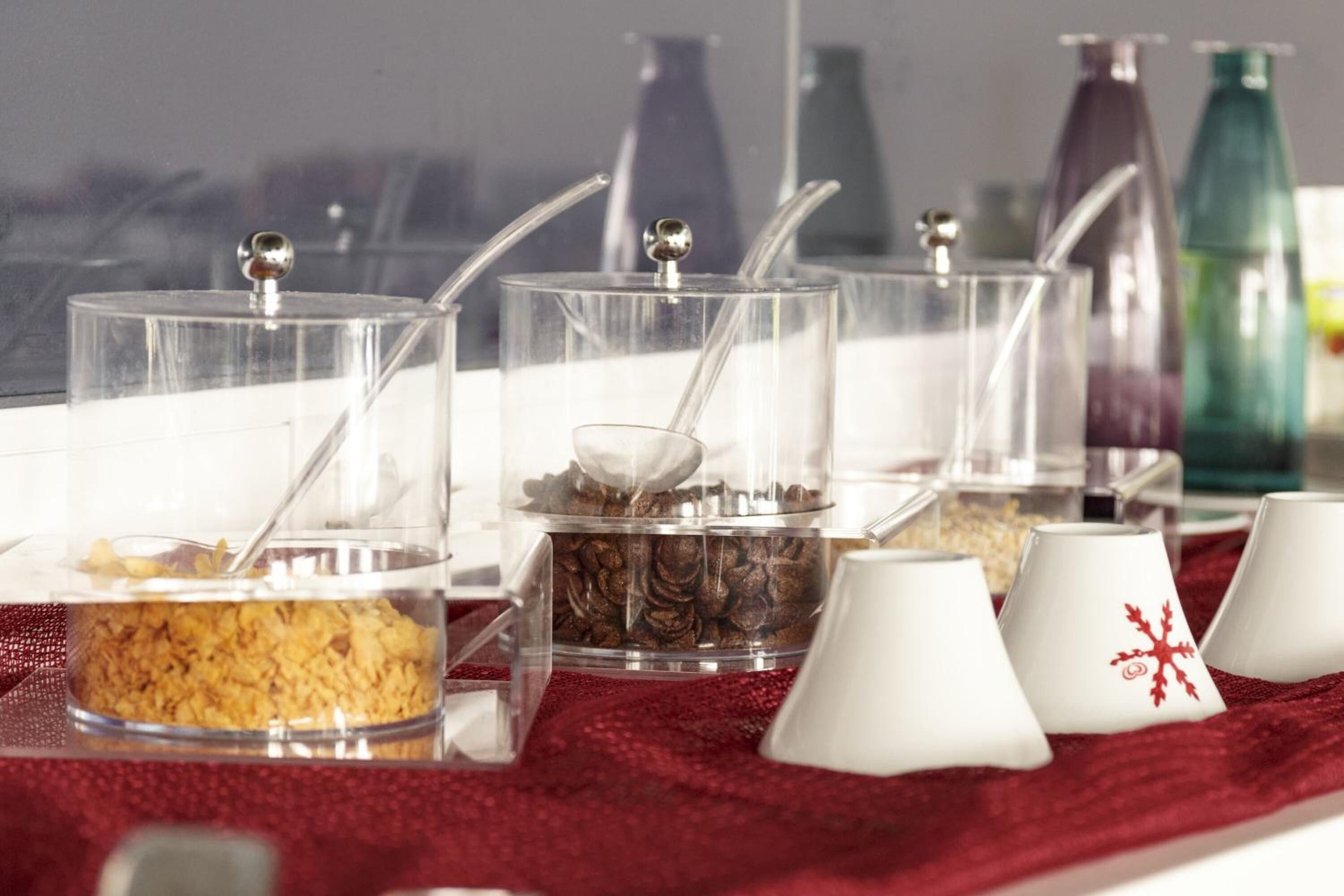 Una mesa de buffet con recipientes transparentes que contienen diversos alimentos y utensilios.