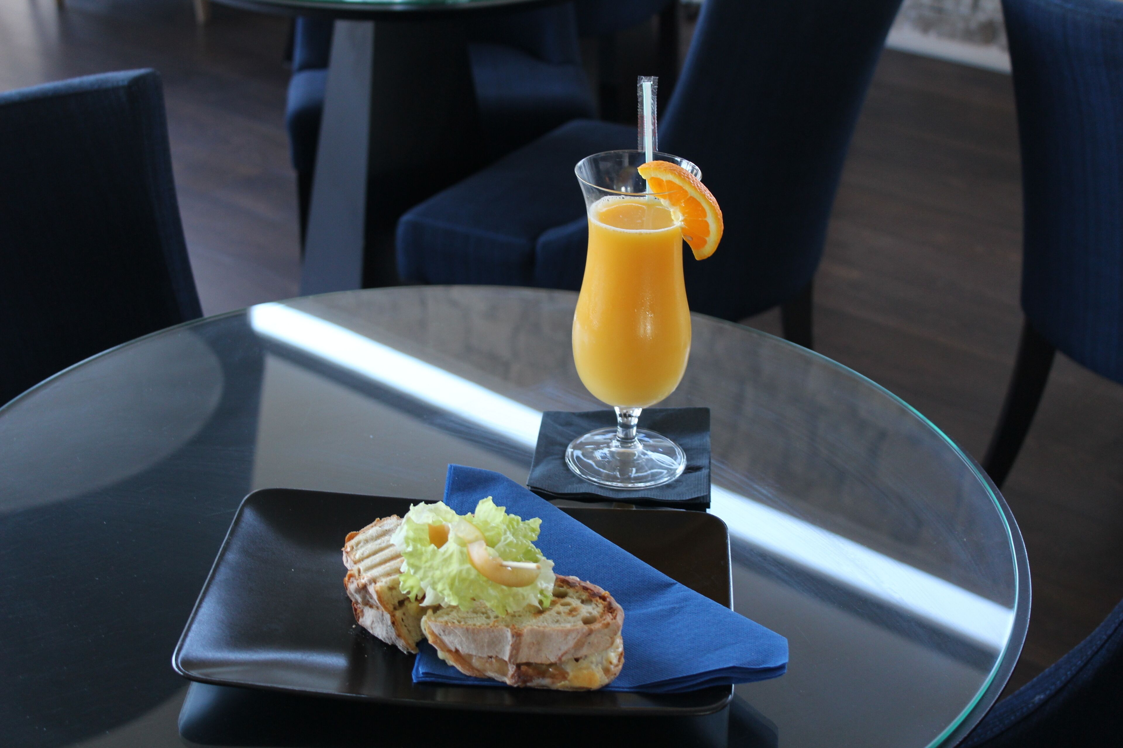 A glass table with a sandwich and a glass of orange juice.