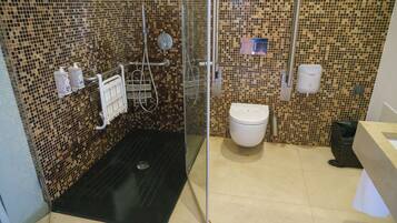 Un baño con pared de mosaicos, cabina de ducha de cristal, inodoro blanco y un cubo de basura.
