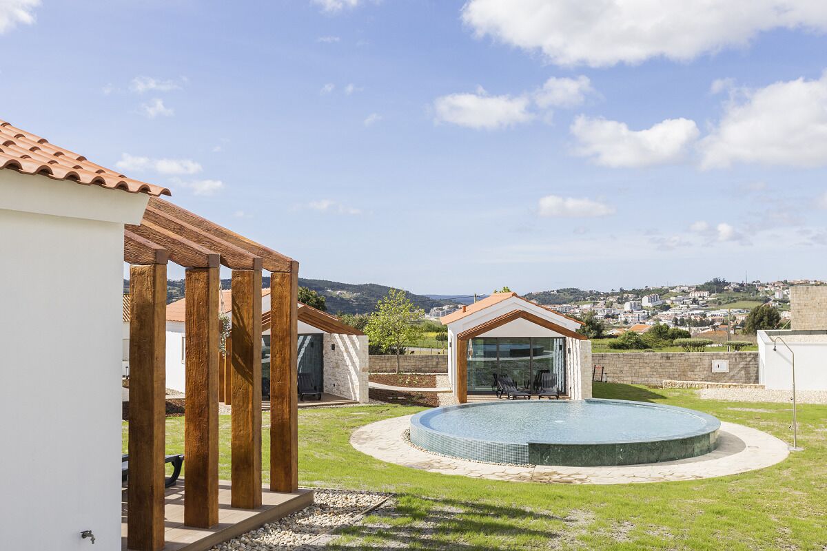 A modern outdoor pool area with a wooden pergola, a glass-enclosed structure, and a view of the surrounding landscape.