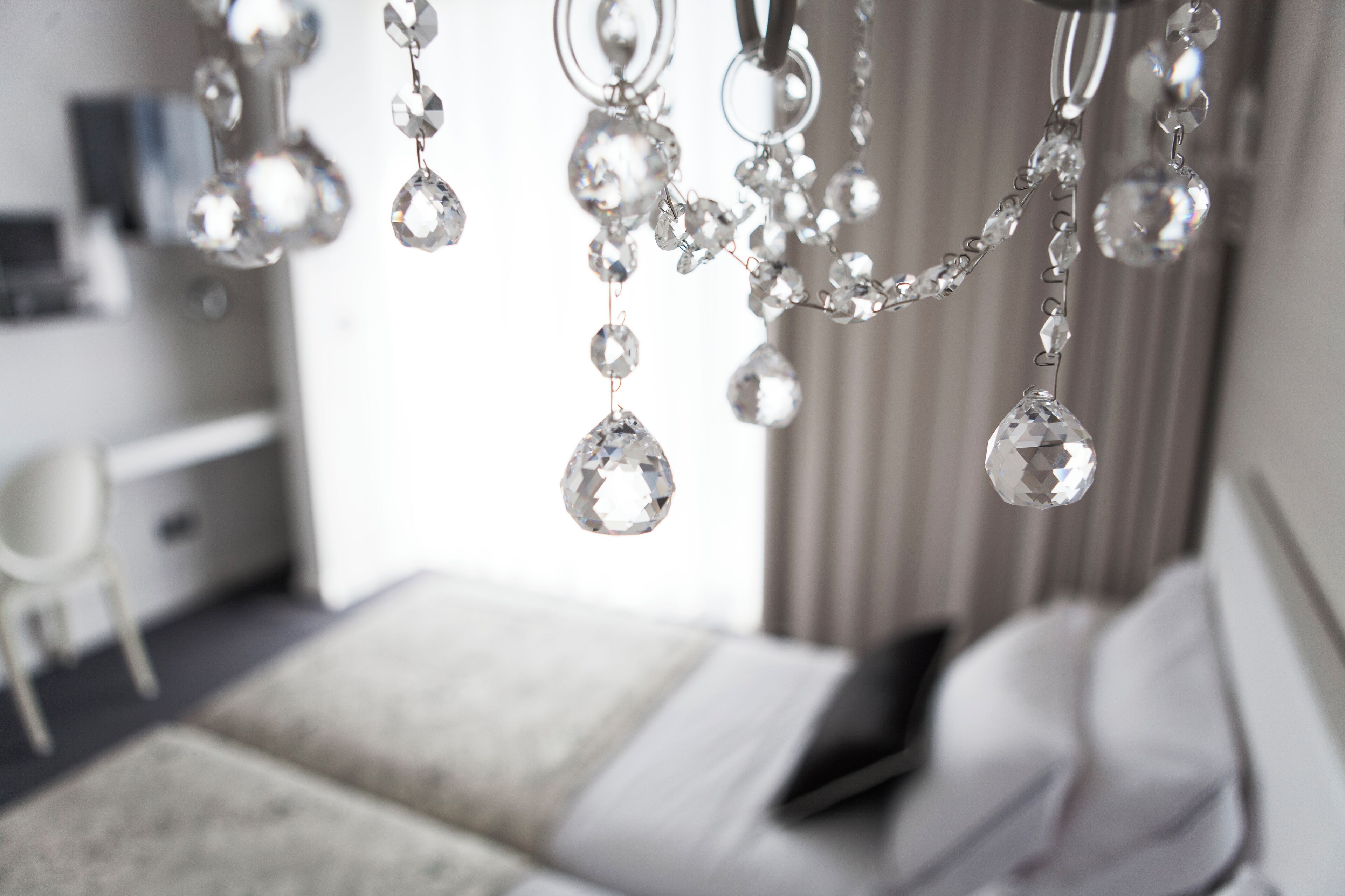 A bedroom with a bed, a bedside table, and a hanging chandelier with crystal decorations.