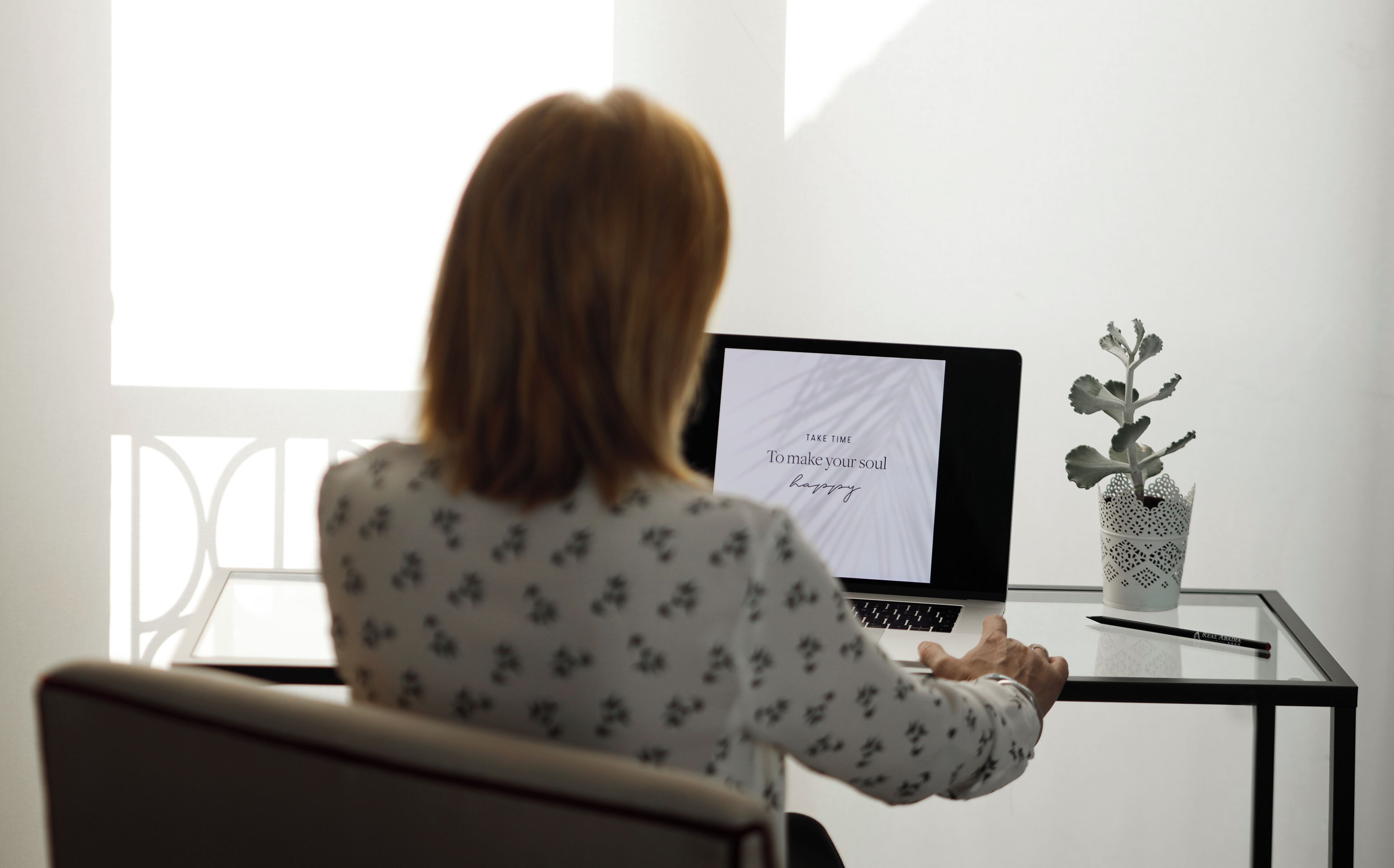 A person sitting at a glass table with a laptop displaying motivational text.