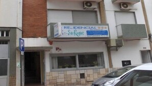 A multi-story residential building with balconies, a visible parking sign, and a signboard advertising a residential property.