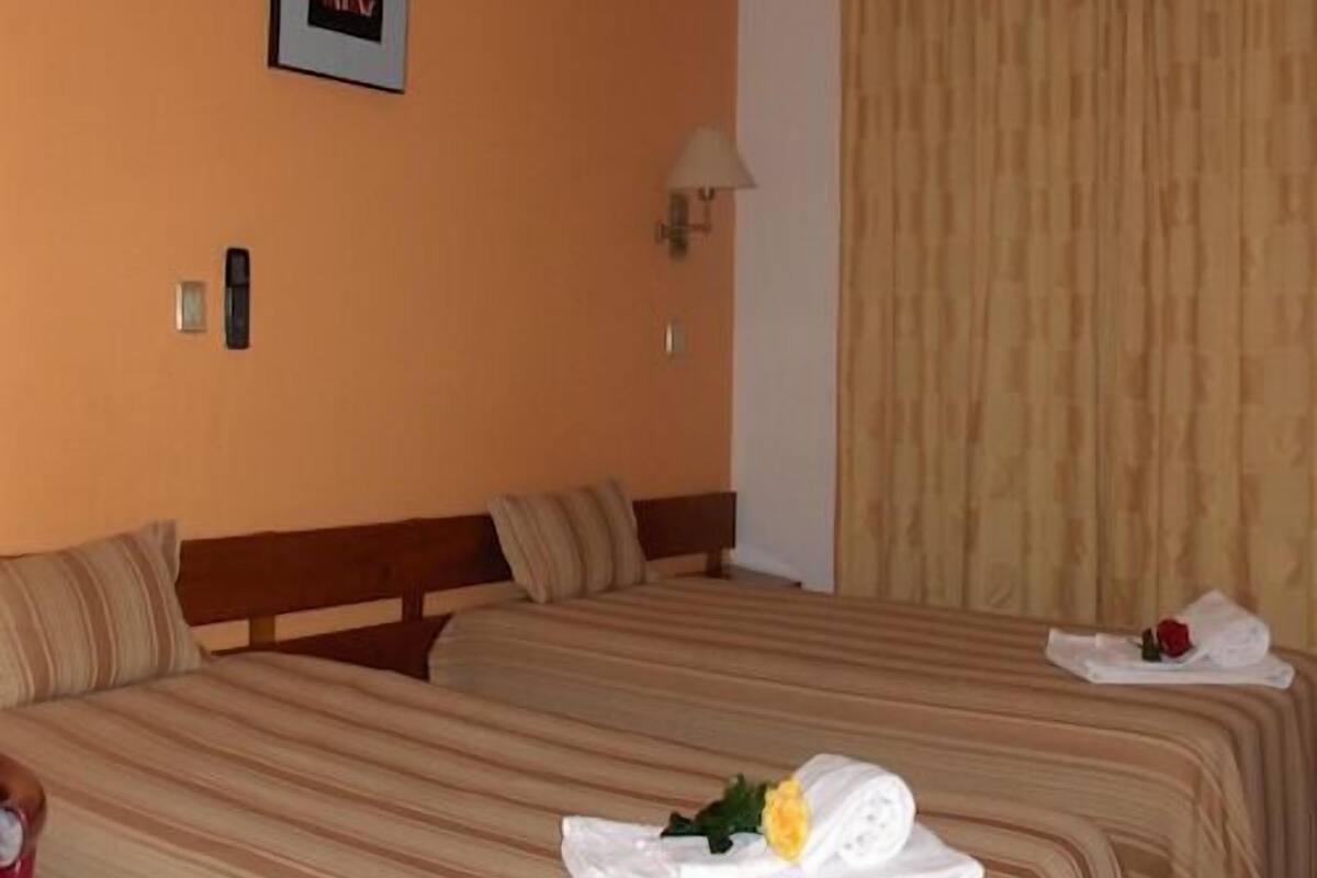A hotel room with two beds, a framed picture on the wall, a lamp, and a window with curtains.