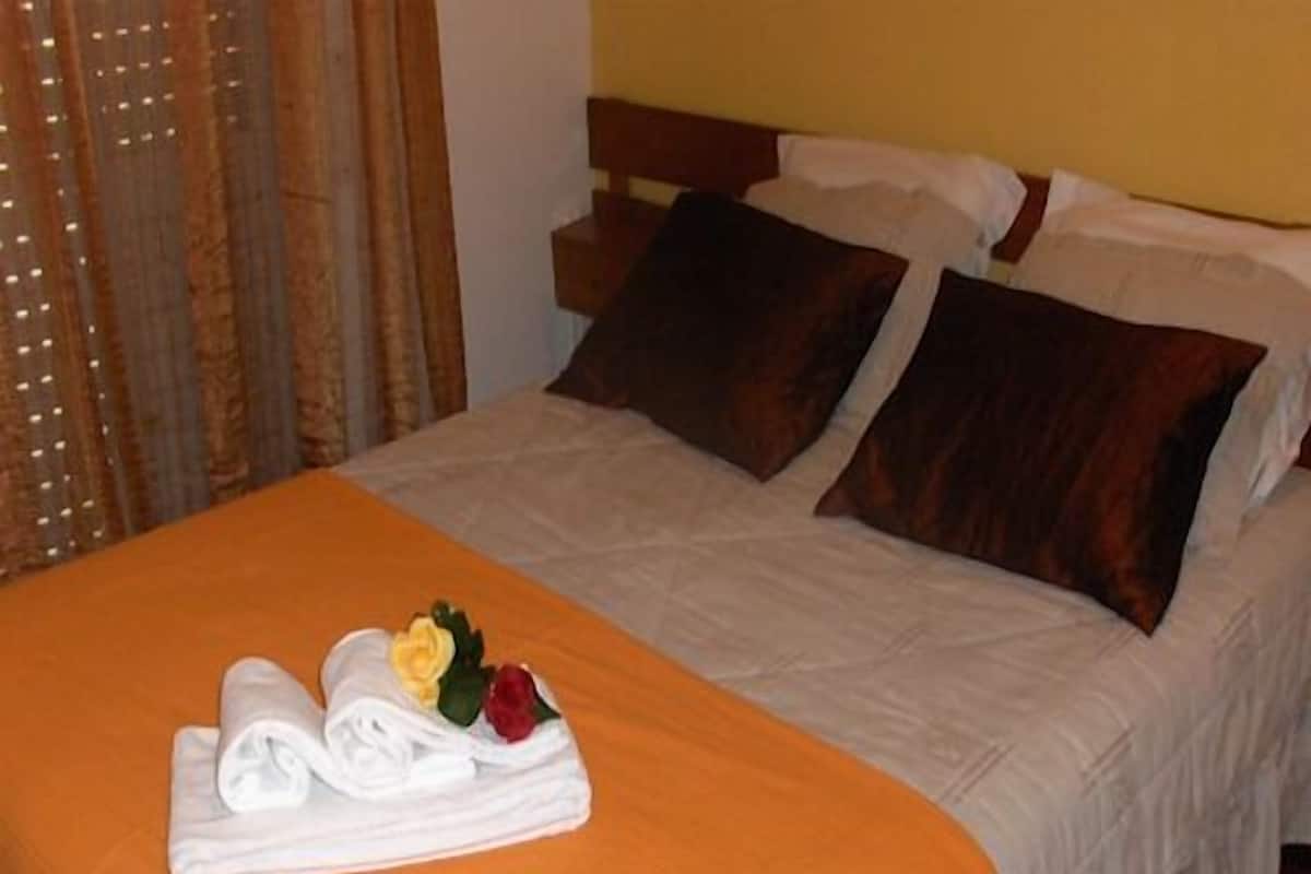 A neatly made bed with a white and orange bedspread, two pillows, and a folded towel with a flower.