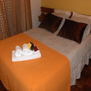 A neatly made bed with a white and orange bedspread, two pillows, and a folded towel with a flower.