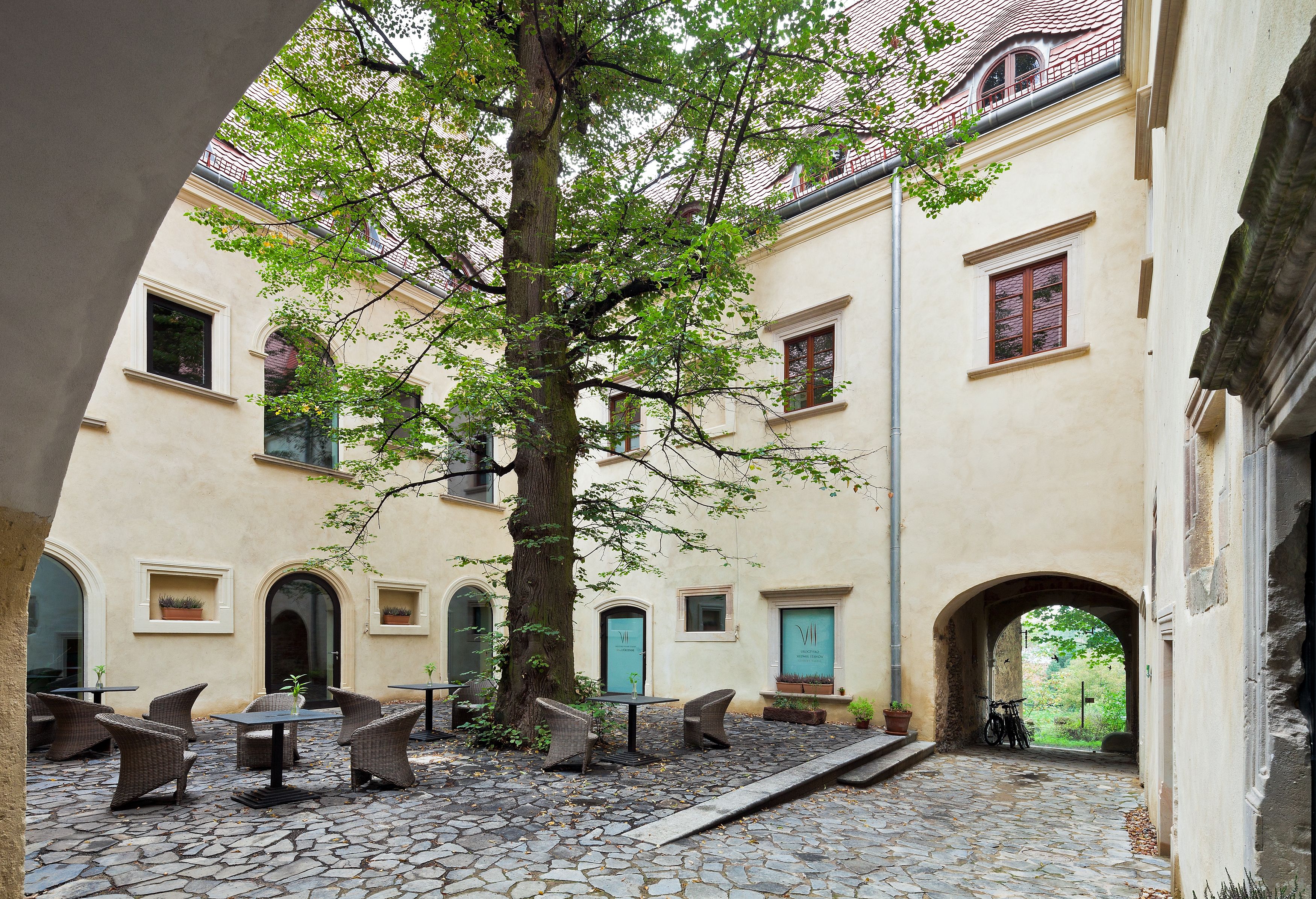 A courtyard with stone flooring, outdoor seating, and a tree.