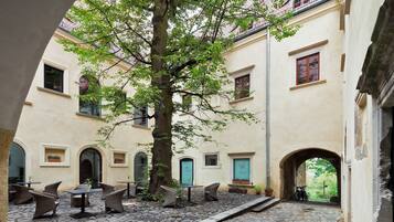 A courtyard with stone flooring, outdoor seating, and a tree.