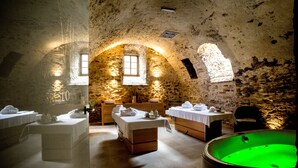 A spa room with a stone wall, a wooden massage table, a massage chair, and a green hot tub. - Uroczysko Siedmiu Stawów & Spa by L'Occitane (Niemcza)