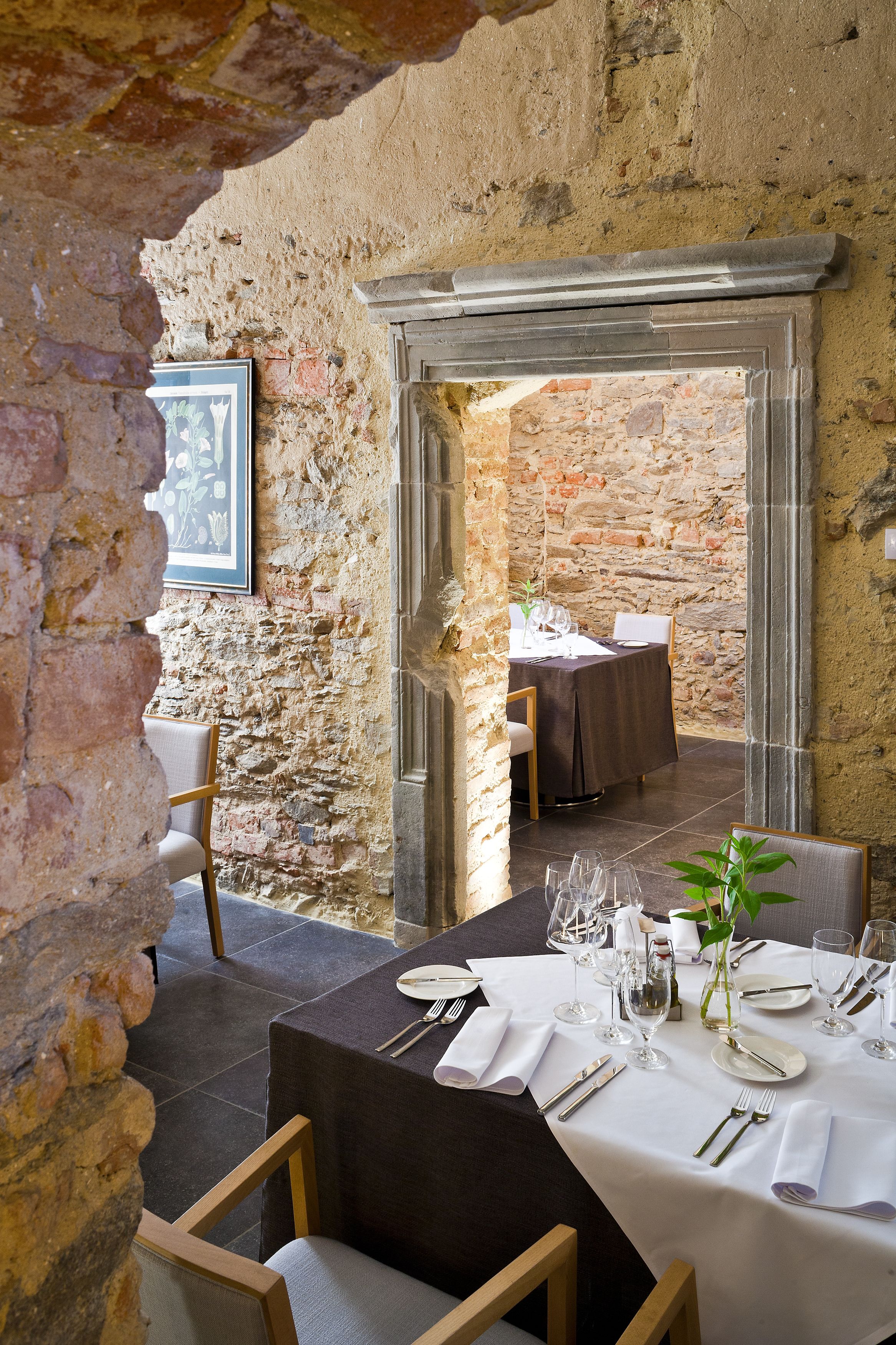 A restaurant with a rustic stone wall, a framed picture, and a table set for dining.
