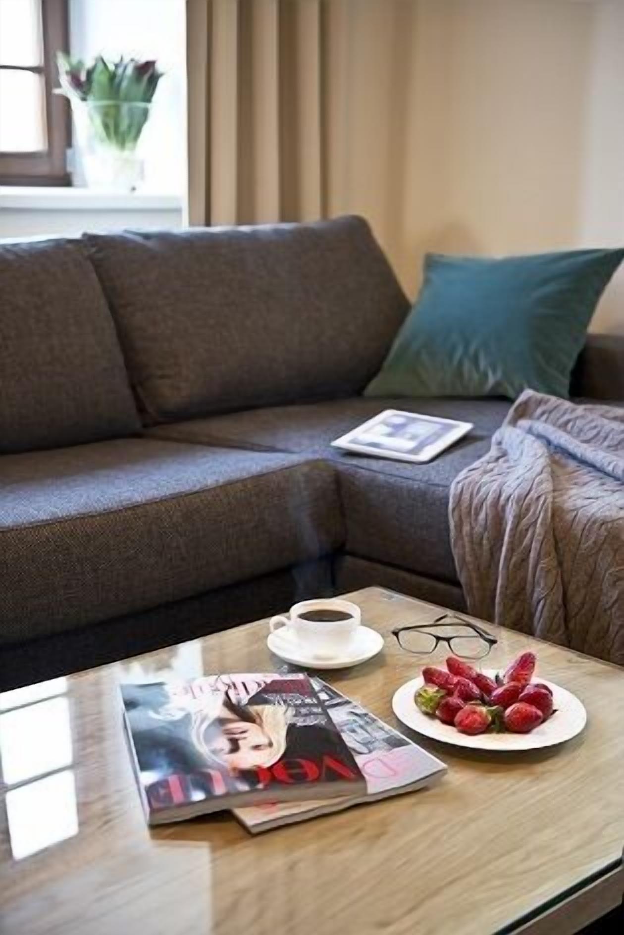 A living room with a sofa, a coffee table with a magazine, a plate of strawberries, and a cup of coffee.