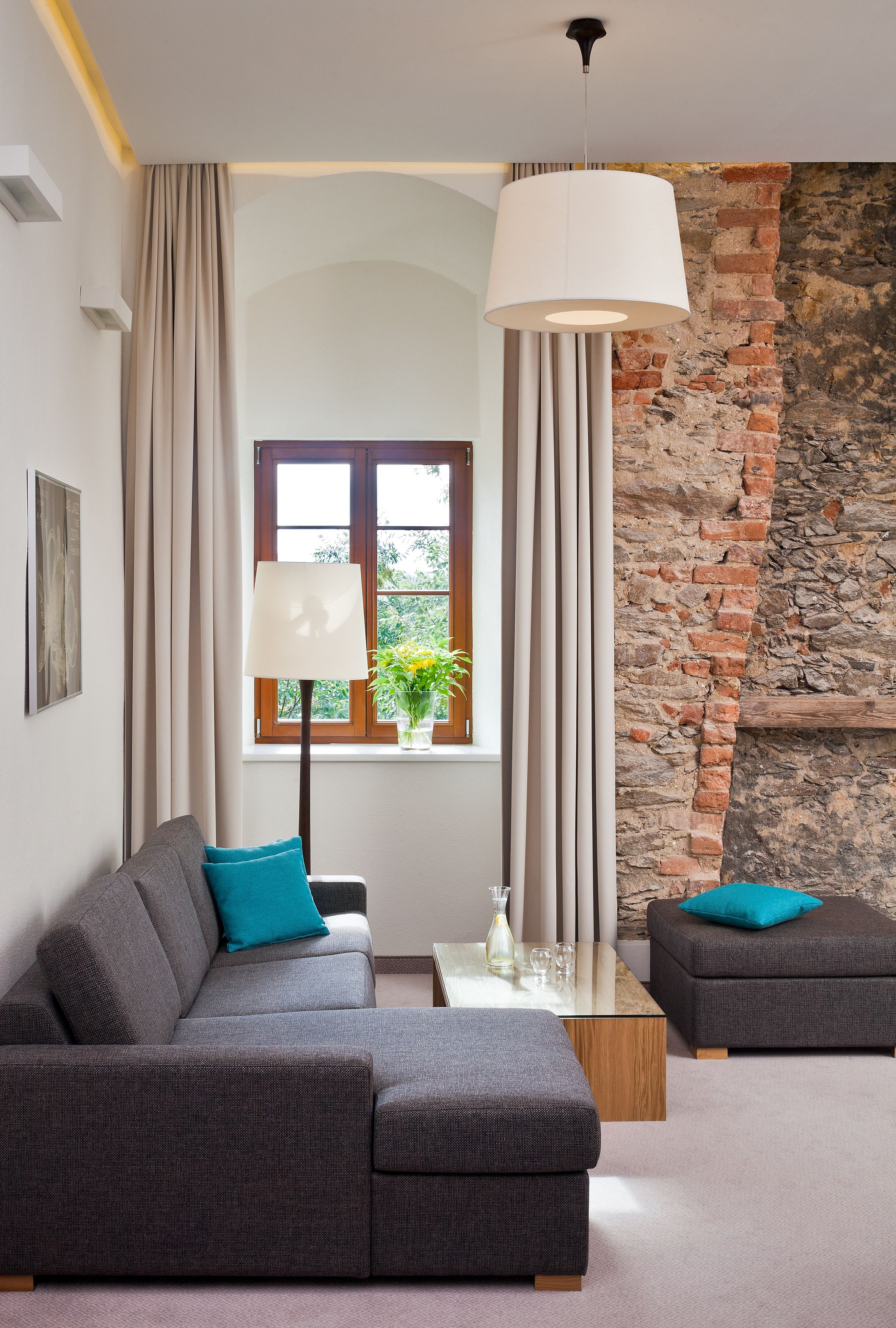A modern living room with a grey sofa, a matching ottoman, a coffee table, a floor lamp, and a view of a brick wall and window.