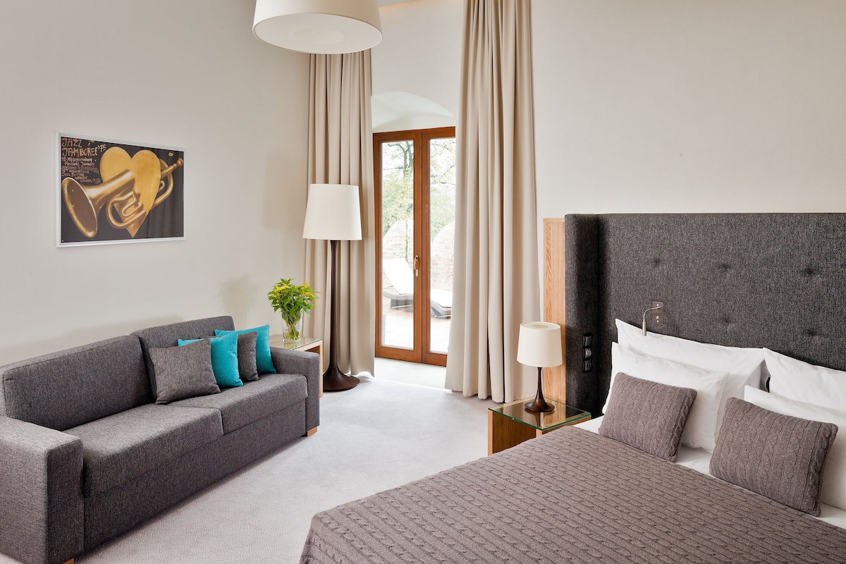 A hotel room with a bed, a sofa, a lamp, and a painting on the wall.