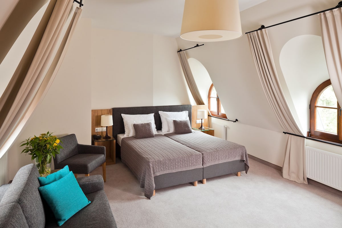 A bedroom with a bed, two nightstands, a chair, and a window with curtains.