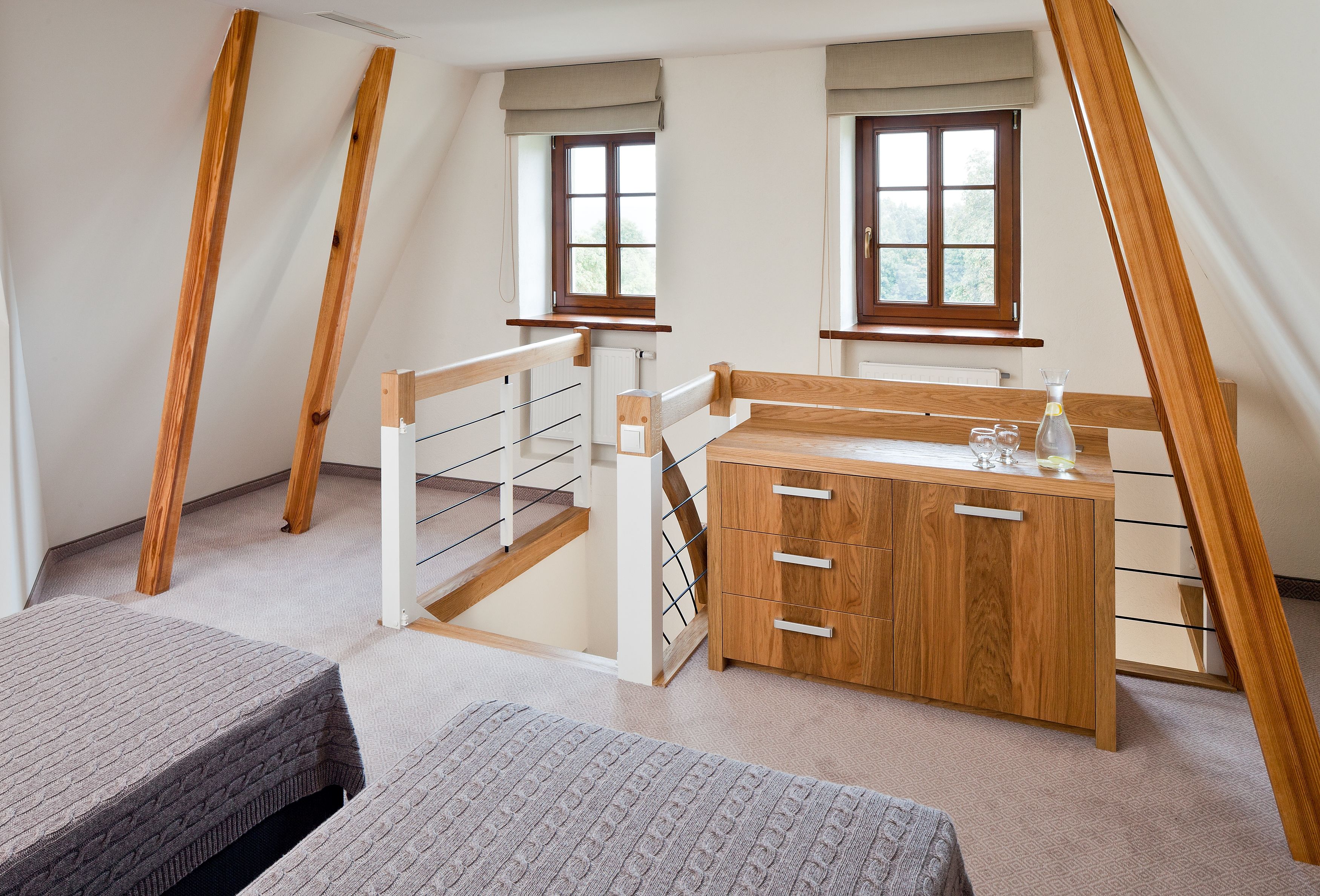 A room with a sloped ceiling, wooden beams, a wooden desk, a radiator, and a window with a view of trees.