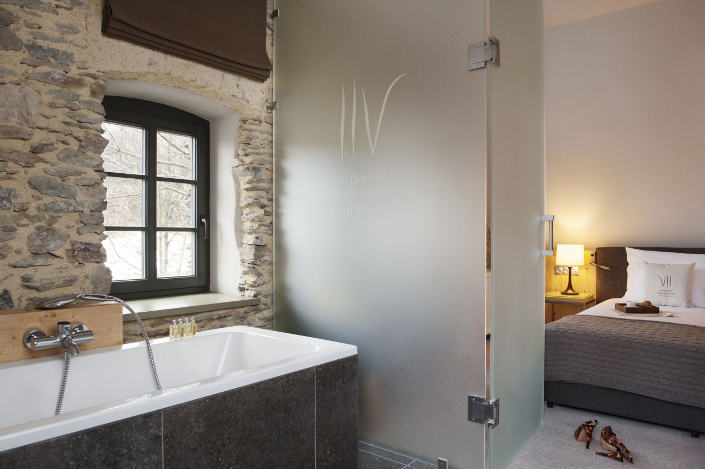Un baño con pared de piedra, una bañera y una ventana.