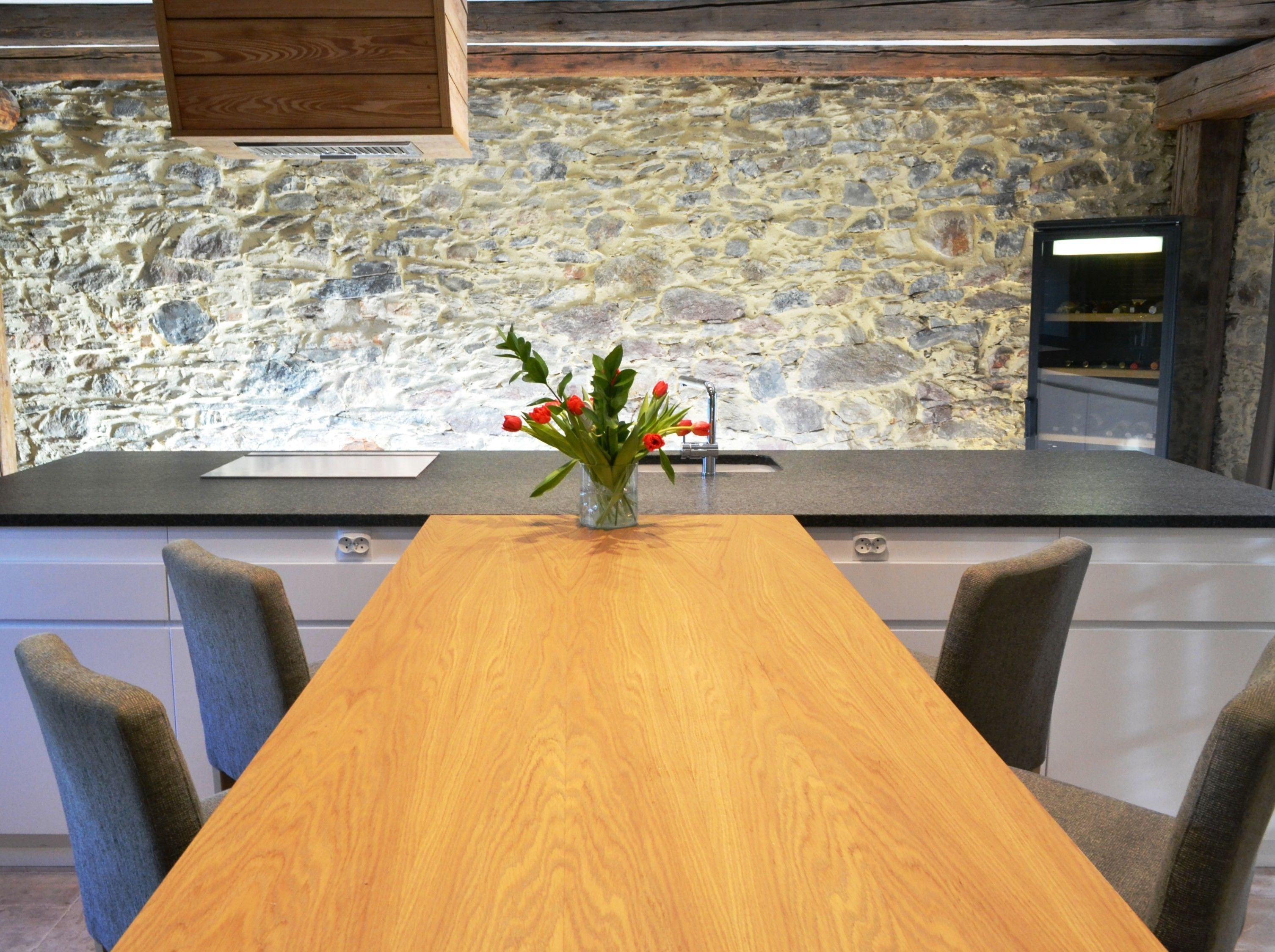A kitchen with a stone wall, a wooden table, and chairs.
