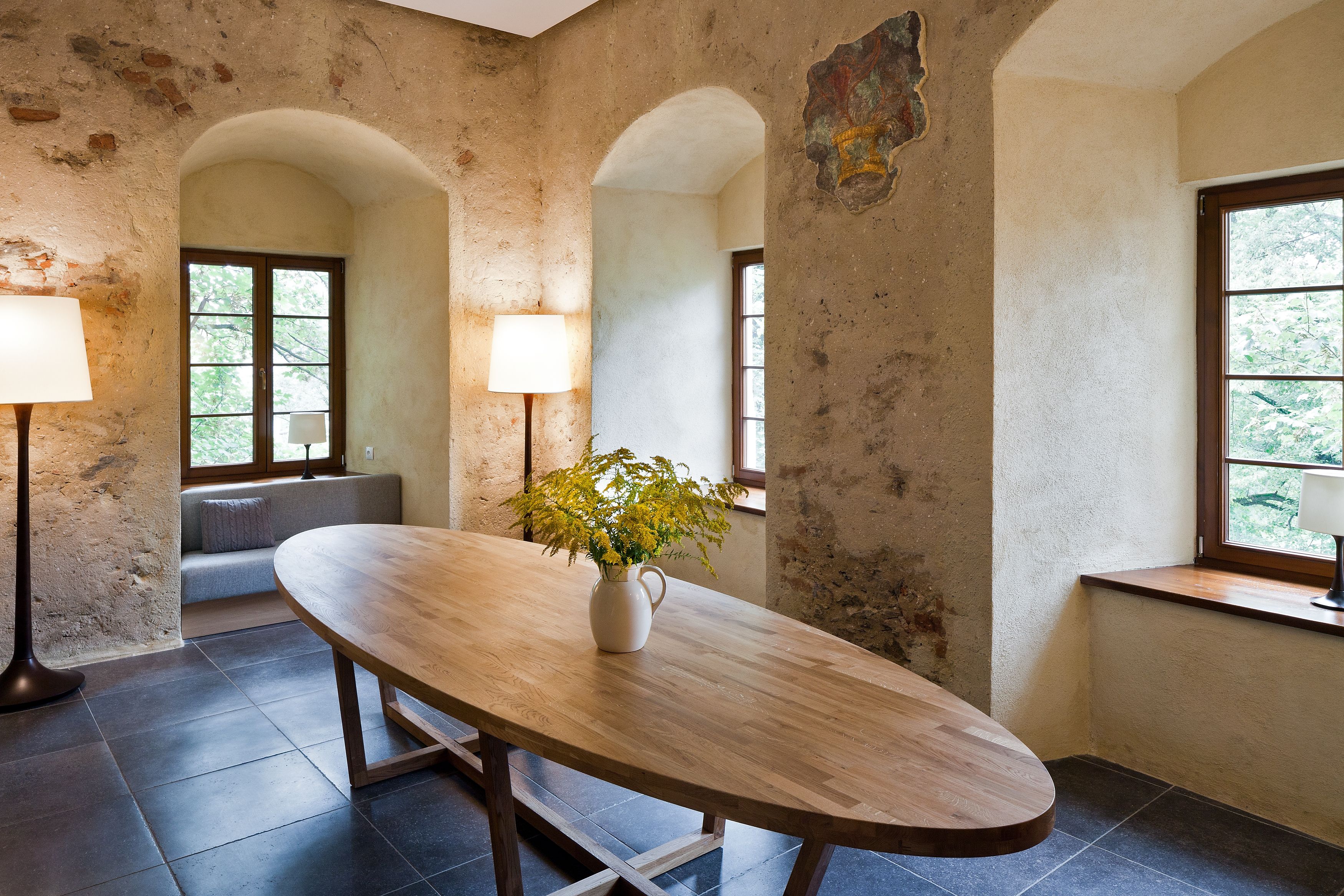 A dining area with a wooden table, two lamps, a vase with flowers, and a bench.