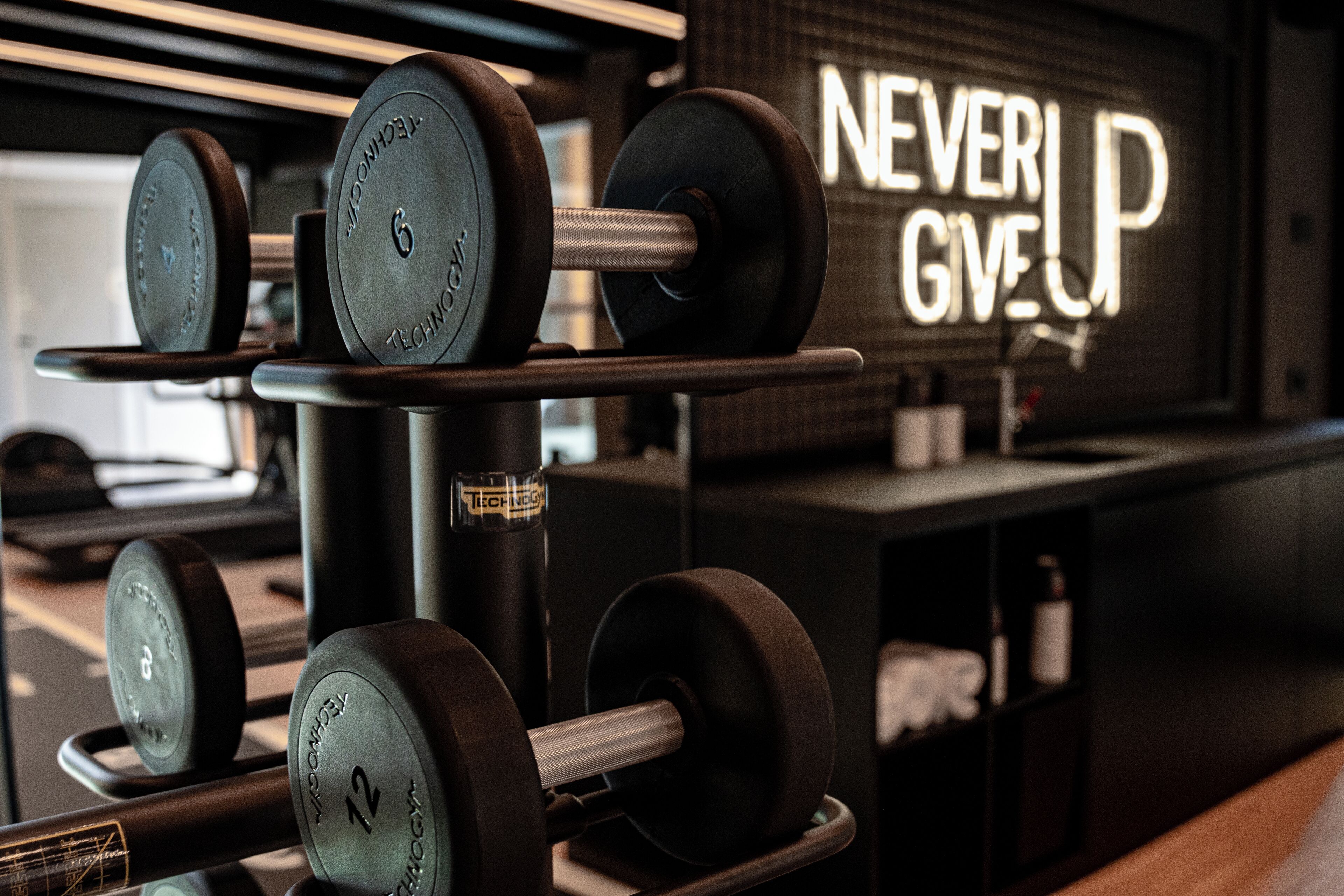 A gym with weightlifting equipment and a motivational sign that reads "NEVER GIVE UP".