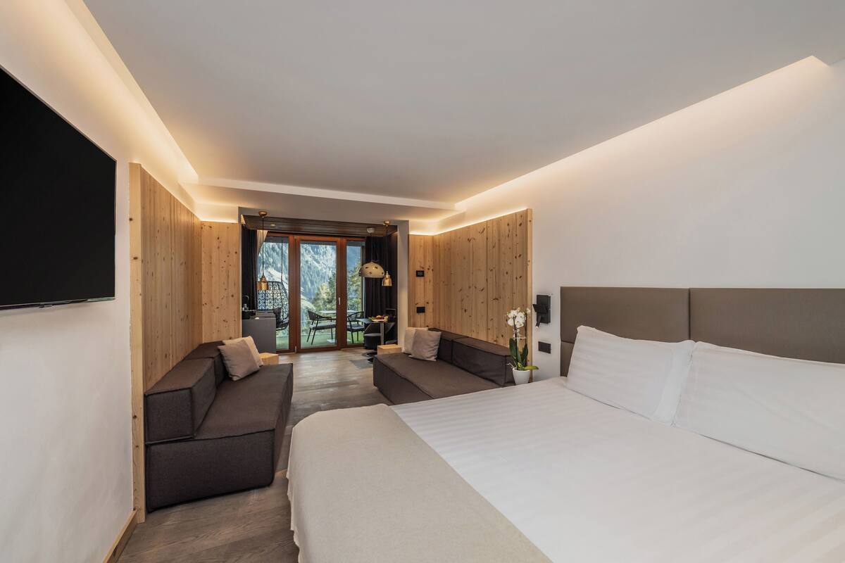 A modern bedroom with a large bed, a sofa, and a dining area with a view.