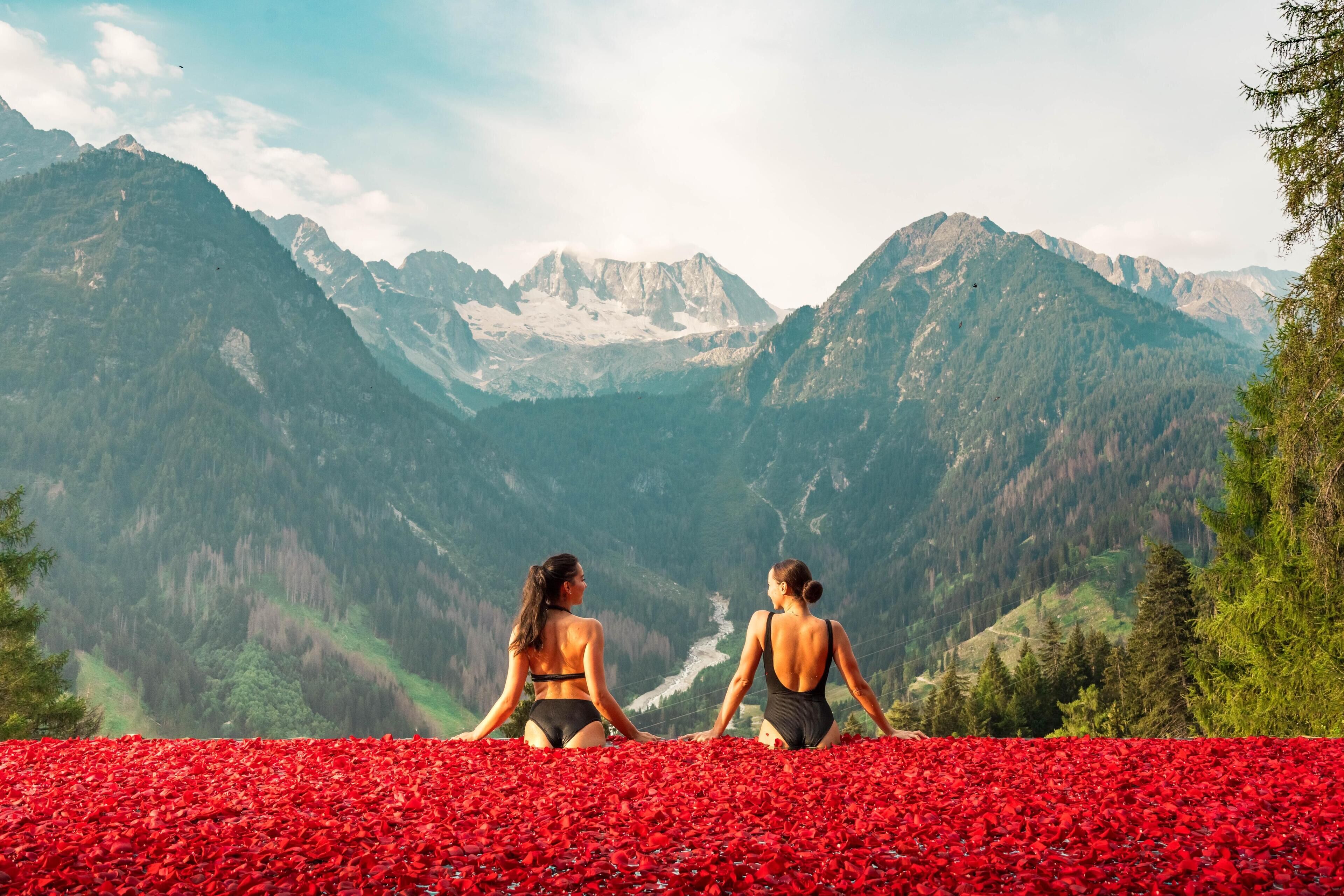Zwei Frauen sitzen auf einem roten Teppich und blicken auf eine gebirgige Landschaft.