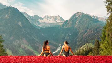 Zwei Frauen sitzen auf einem roten Teppich und blicken auf eine gebirgige Landschaft.