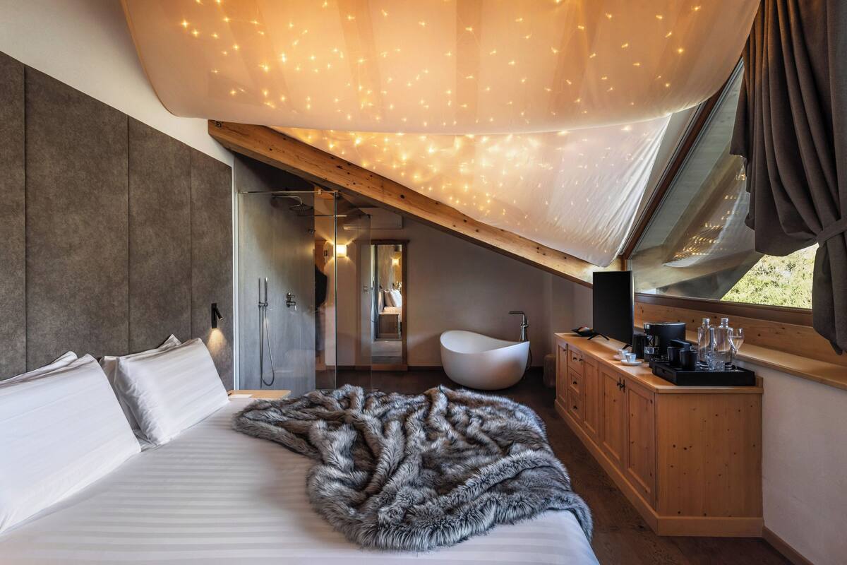 A modern bedroom with a large bed, a fur throw, a wooden cabinet, and a bathroom with a white sink and shower.