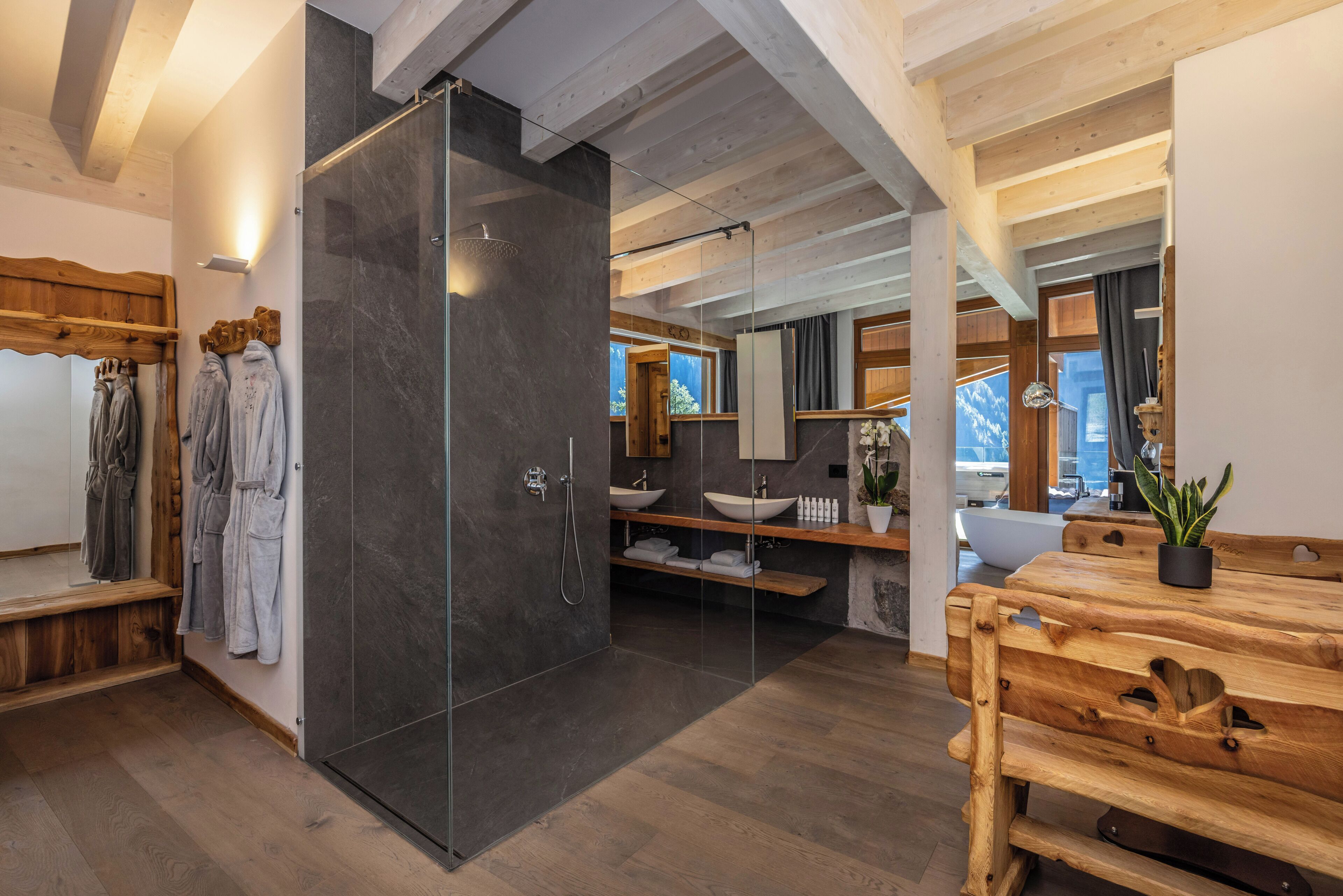 A modern bathroom with a glass shower enclosure, wooden benches, and a wooden vanity with a sink.