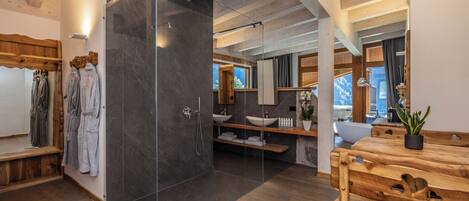 A modern bathroom with a glass shower enclosure, wooden benches, and a wooden vanity with a sink.