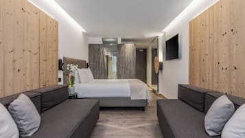 Une chambre d’hôtel moderne avec un grand lit, deux canapés, des murs recouverts de panneaux en bois, un téléviseur à écran plat et une plante en pot.