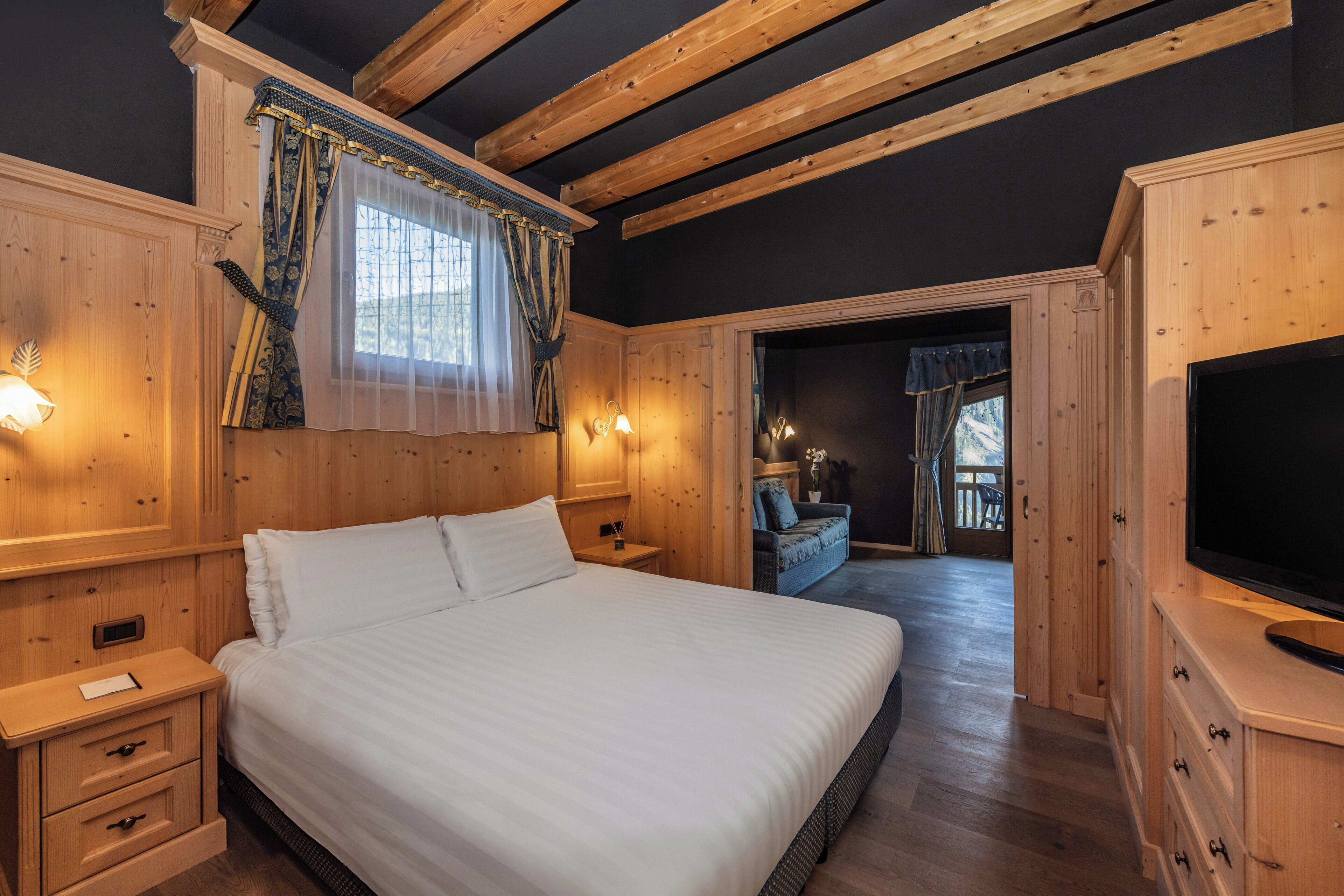 A wooden bedroom with a large bed, bedside lamps, and a TV on a wooden cabinet.