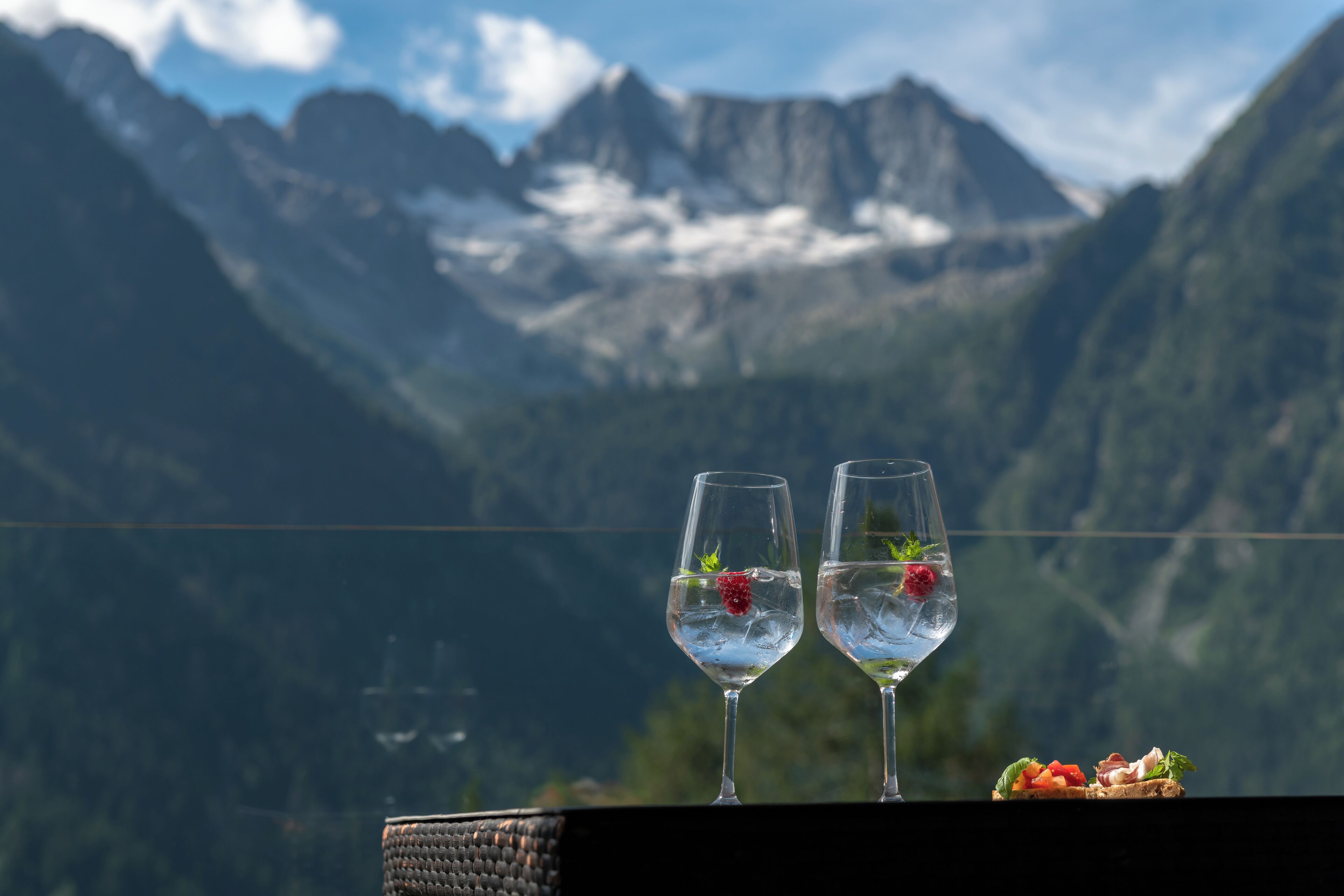 Due bicchieri d'acqua con frutti di bosco su un balcone con vista sulle montagne.