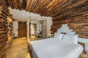 A room with a wooden log wall, a large bed with white bedding, and a glass shower enclosure. - Hotel Chalet Al Foss (Adults Only) (Vermiglio)
