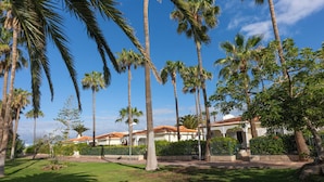 A courtyard with tall palm trees, a building with a tiled roof, and a well-maintained lawn. - Ona Sueño Azul (Adeje)