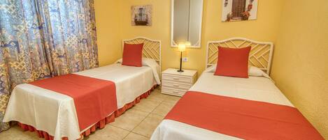 A hotel room with two beds, each with a red and white bedspread, a nightstand with a lamp, and a mirror on the wall.