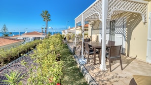 A patio area with a table and chairs, surrounded by a white lattice structure, overlooking a coastal view. - Ona Sueño Azul (Adeje)