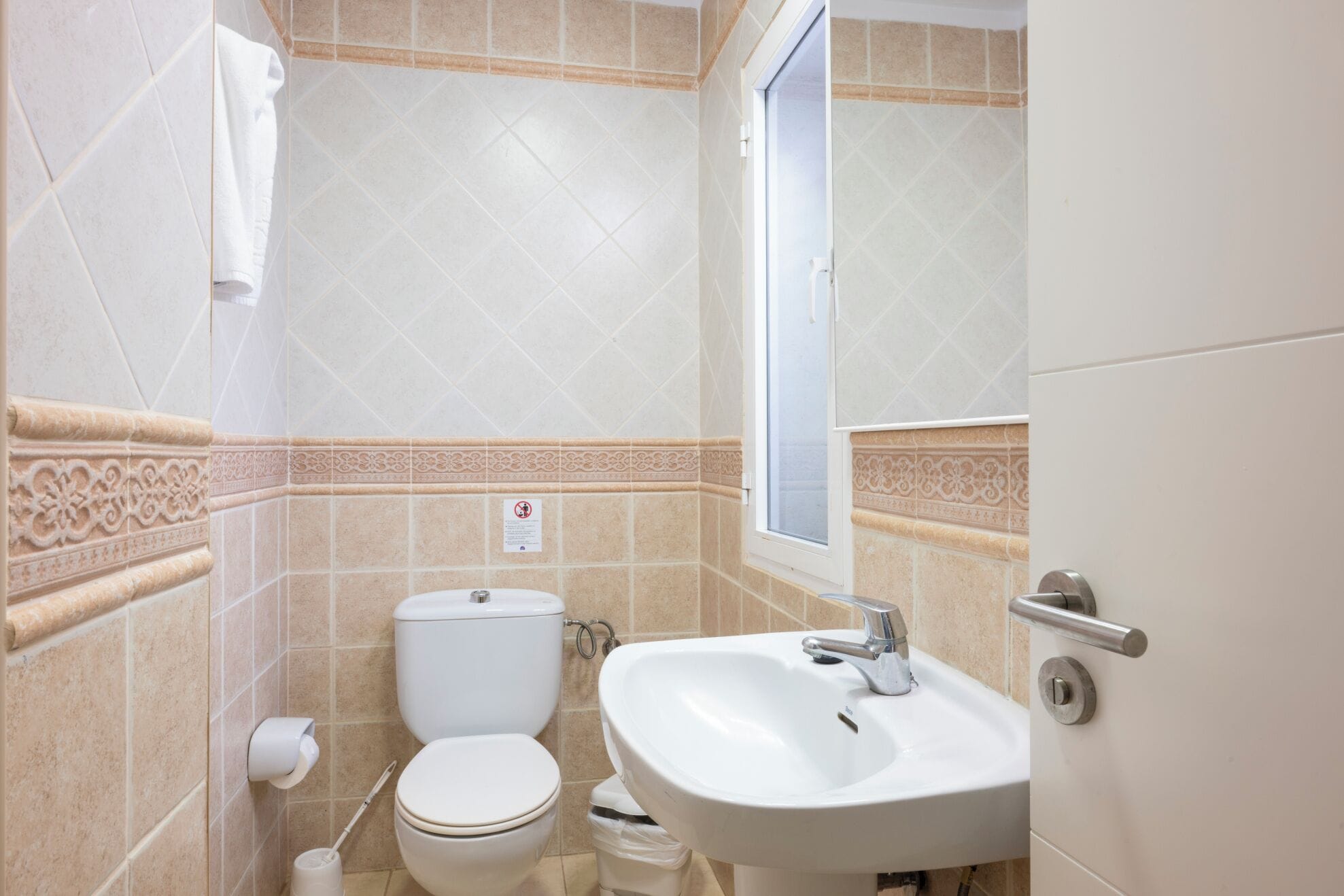 A bathroom with a toilet, sink, and a window.