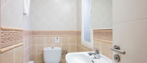 A bathroom with a toilet, sink, and a window.