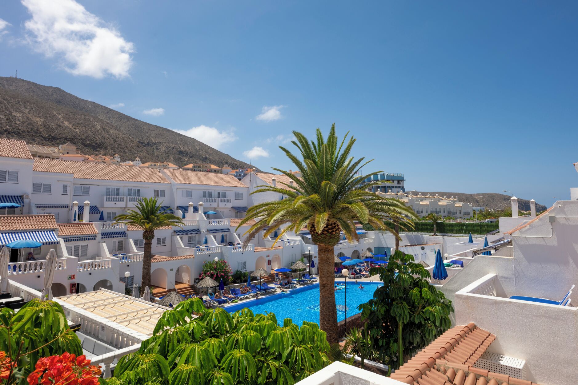 A resort with a swimming pool, palm trees, and Mediterranean-style buildings.