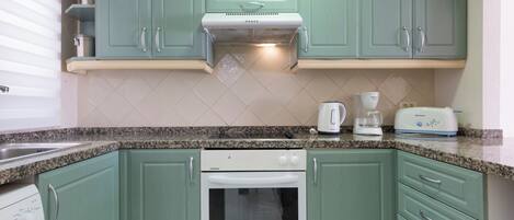 A kitchen with green cabinets, a white oven, a coffee maker, and a toaster.