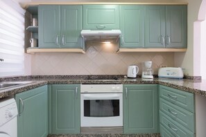 Una cocina con gabinetes verdes, horno blanco, cafetera y tostadora.