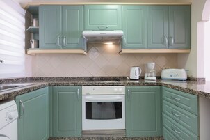 Una cocina con gabinetes verdes, horno blanco, cafetera y tostadora.