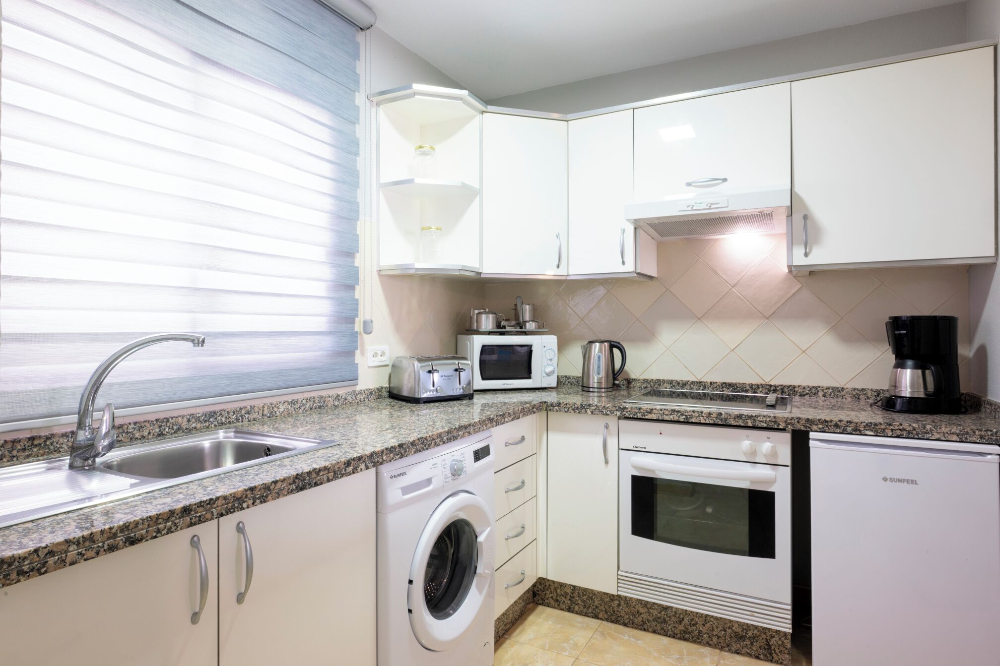 A compact kitchen with a washing machine, a microwave, a toaster, and a coffee maker.