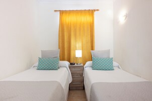 Habitación de hotel con dos camas, una mesita de noche, una lámpara y una ventana con cortinas.