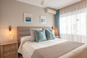 Une chambre à coucher comprenant un lit, des tables de chevet, un climatiseur fixé au mur et des rideaux.
