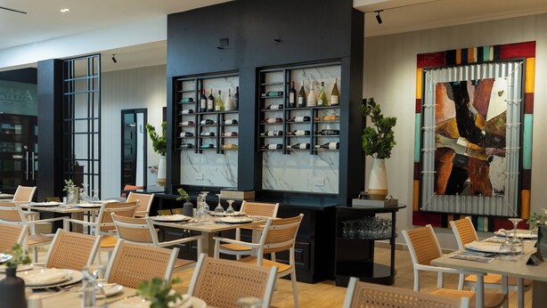 Un interior de restaurante moderno con varias mesas, sillas de mimbre y estanterías para vino en las paredes.