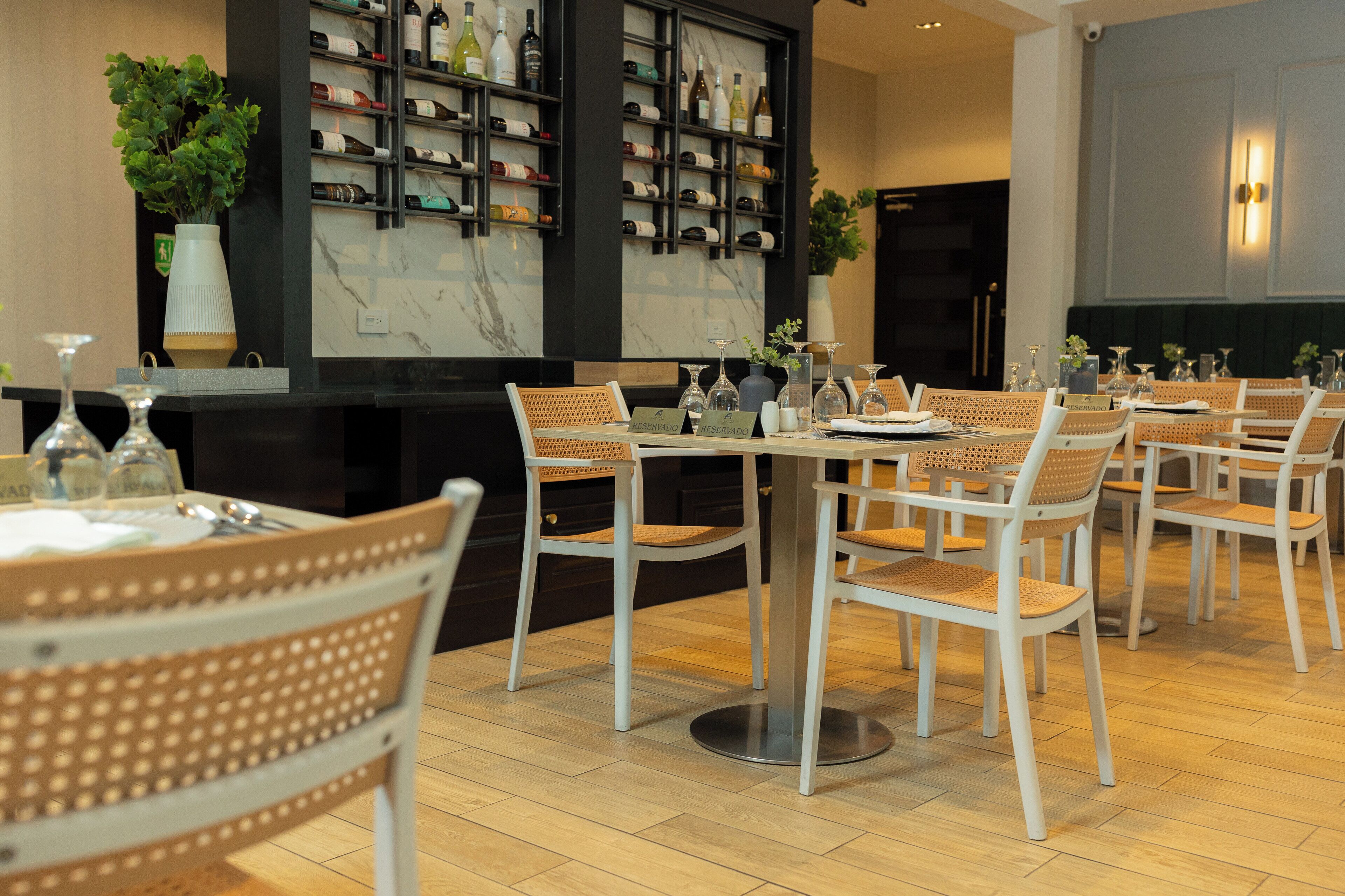 A restaurant with white chairs and tables, a wine rack, and a potted plant.